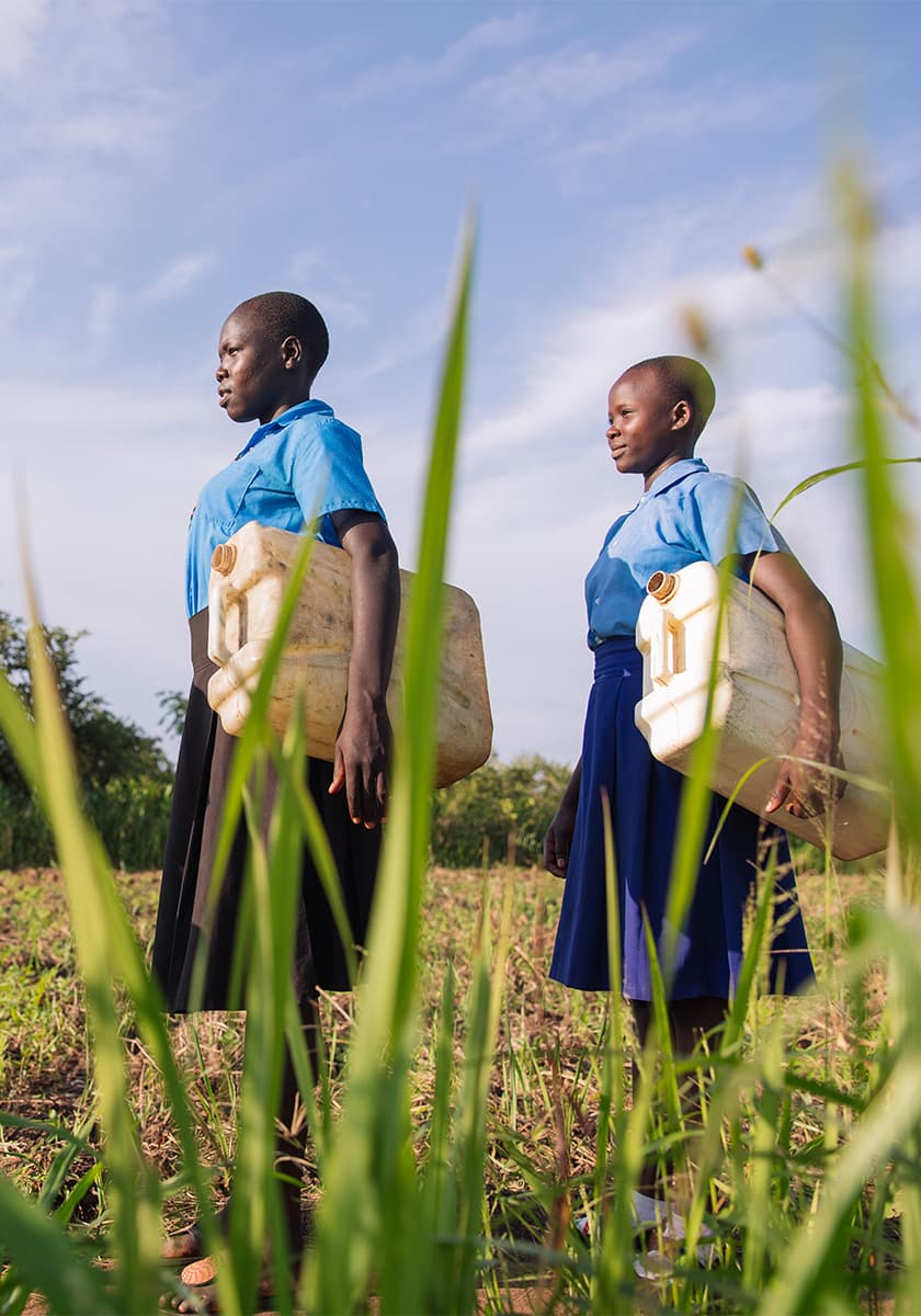 Zwei schwarze Frauen mit Wasserkanistern auf einem Feld.